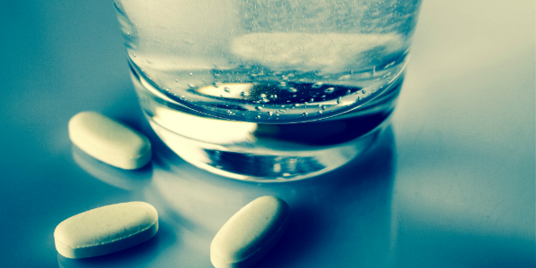 Billede af piller ved siden af et glas vand