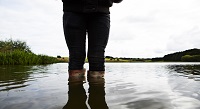 Person i gummistøvler der står i vand til knæene